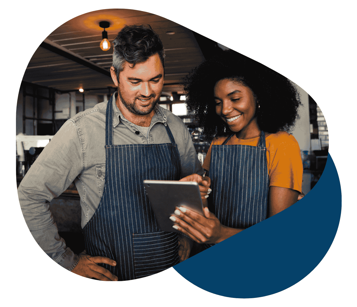 Two restaurant staff in aprons reviewing tablet Two restaurant staff in aprons reviewing tablet